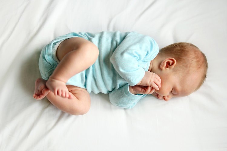 Az édes újszülött baba fehér ágyon alszik