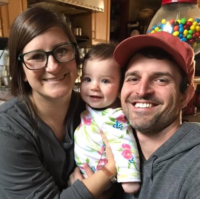 A young mother and father smiling and holding their baby.