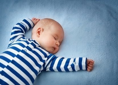 Restful baby sleeping on a blue bed with blue and white striped pajamas.