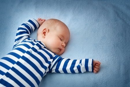 Restful baby sleeping on a blue bed with blue and white striped pajamas.
