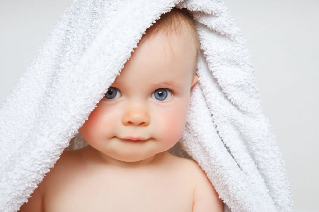 Infant with a white towel draper over its head.