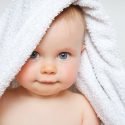 Infant with a white towel draper over its head.