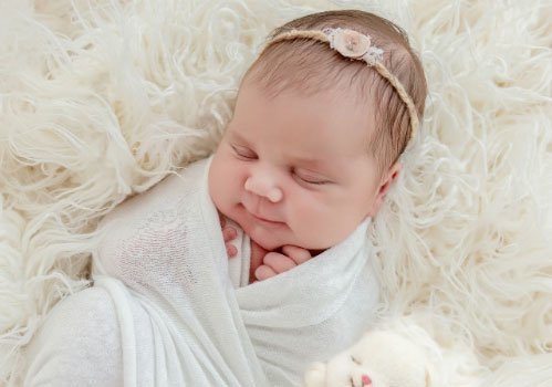 Infant girl sleeping in a swaddle with pink rose hair band
