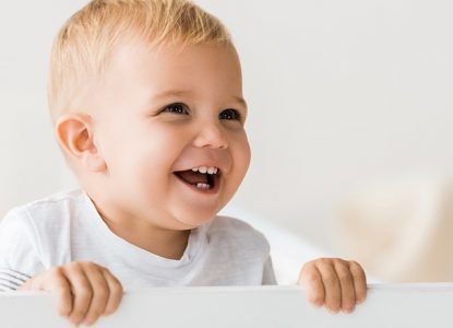Cheerful Toddler Standing In Baby Crib On White Background