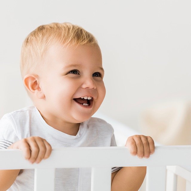 Cheerful Toddler Standing In Baby Crib On White Background